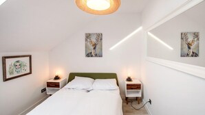 A bedroom with a bed, two bedside tables with lamps, a woven ceiling light fixture, and two wall-mounted paintings.