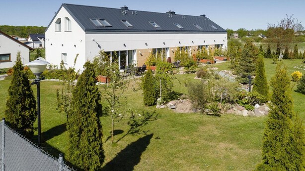 A modern building with a flat roof, multiple windows, and a well-maintained garden with various trees and shrubs.