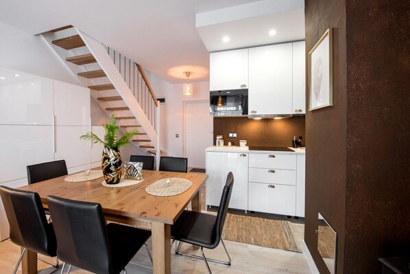 A modern kitchen with white cabinets, a wooden dining table with chairs, and a staircase.