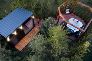 Una cabaña moderna con terraza, jacuzzi y un pequeño espacio para sentarse al aire libre rodeado de árboles.