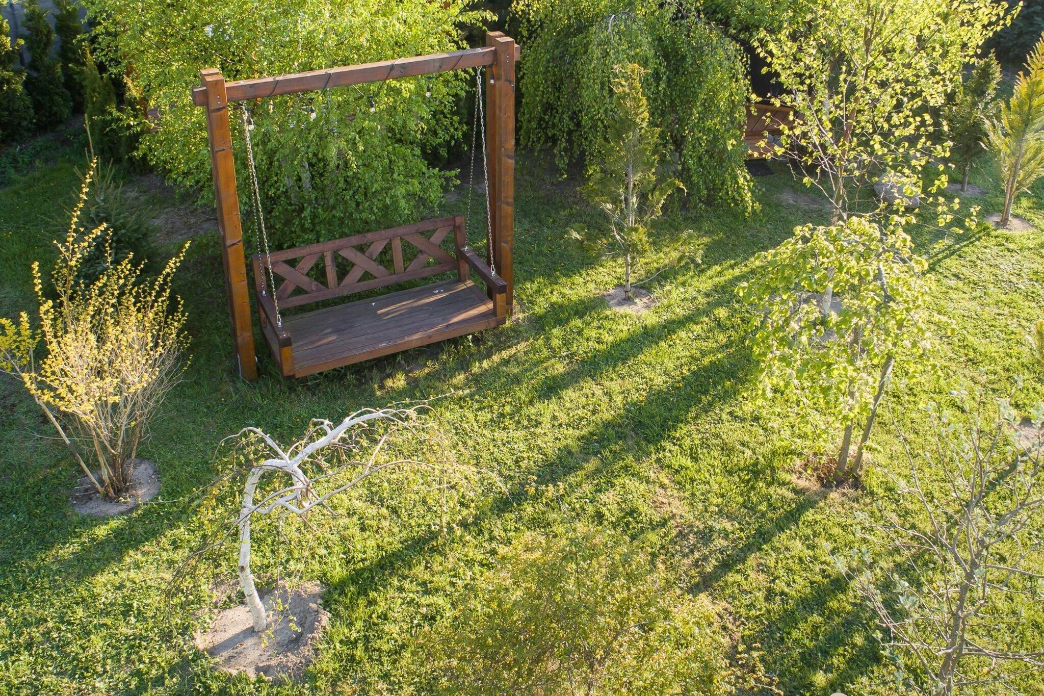 Ein hölzernes Schaukelgerüst in einem Garten mit Gras und kleinen Bäumen.