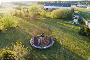 Een trampoline in een grasveld, met een huis en bomen op de achtergrond.