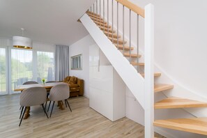 Un interior modern amb una escala, terres de fusta, una zona de menjador amb cadires i un sofà.