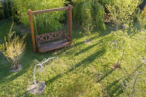 Een houten schommel in een tuin met gras en kleine bomen.
