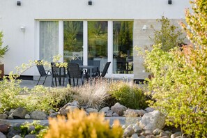 A modern building with a patio area featuring outdoor seating and a garden with rocks and plants.