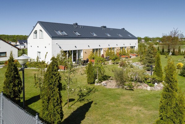 A modern building with a flat roof, multiple windows, and a well-maintained garden with various trees and shrubs.