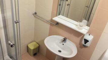 A bathroom with a glass shower enclosure, a white sink with a mirror above it, a toilet, and a small stool.