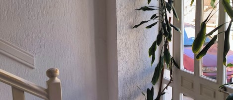A corner of a room with a white textured wall, a wooden railing, and potted plants near a window.