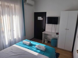 A hotel room with a bed, a desk, a wardrobe, a television, and a window with curtains.