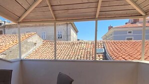 Une terrasse couverte, dotée d’une table et de chaises, qui offre une vue sur le paysage urbain avec ses toits en tuiles rouges.