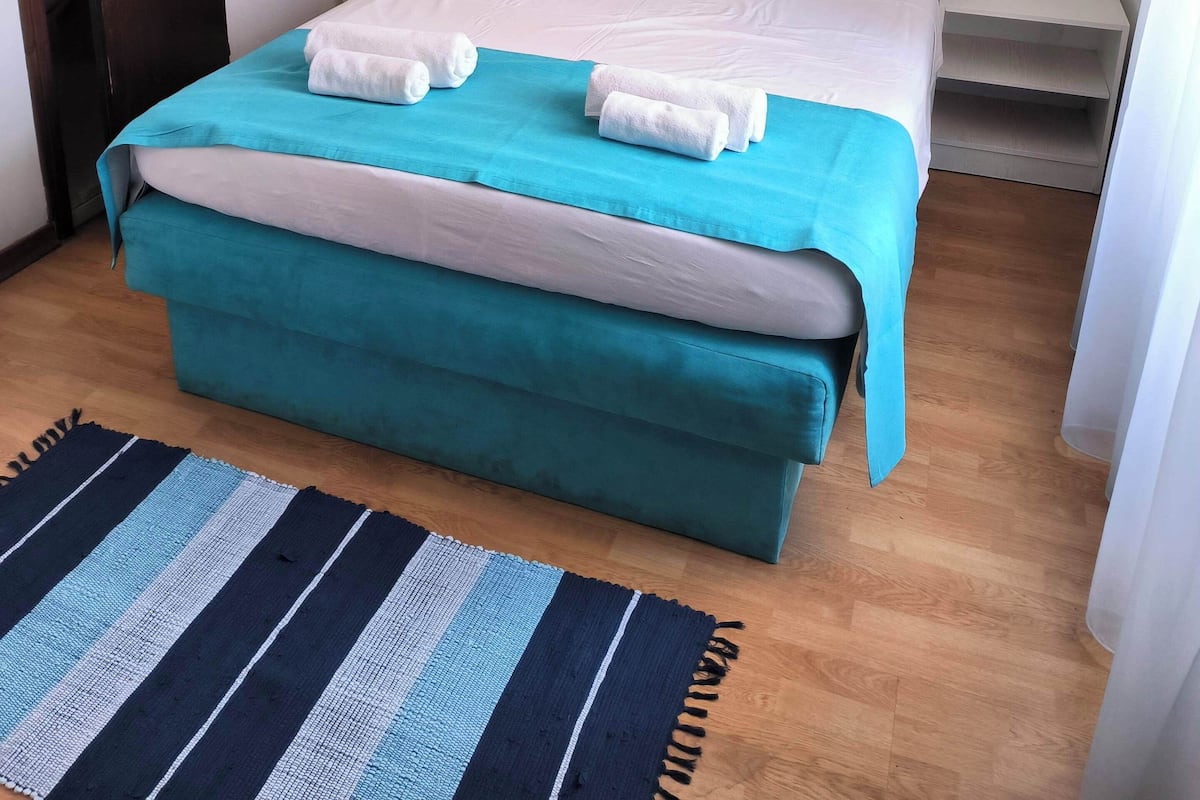 A neatly arranged bedroom with a bed, pillows, and a painting on the wall.