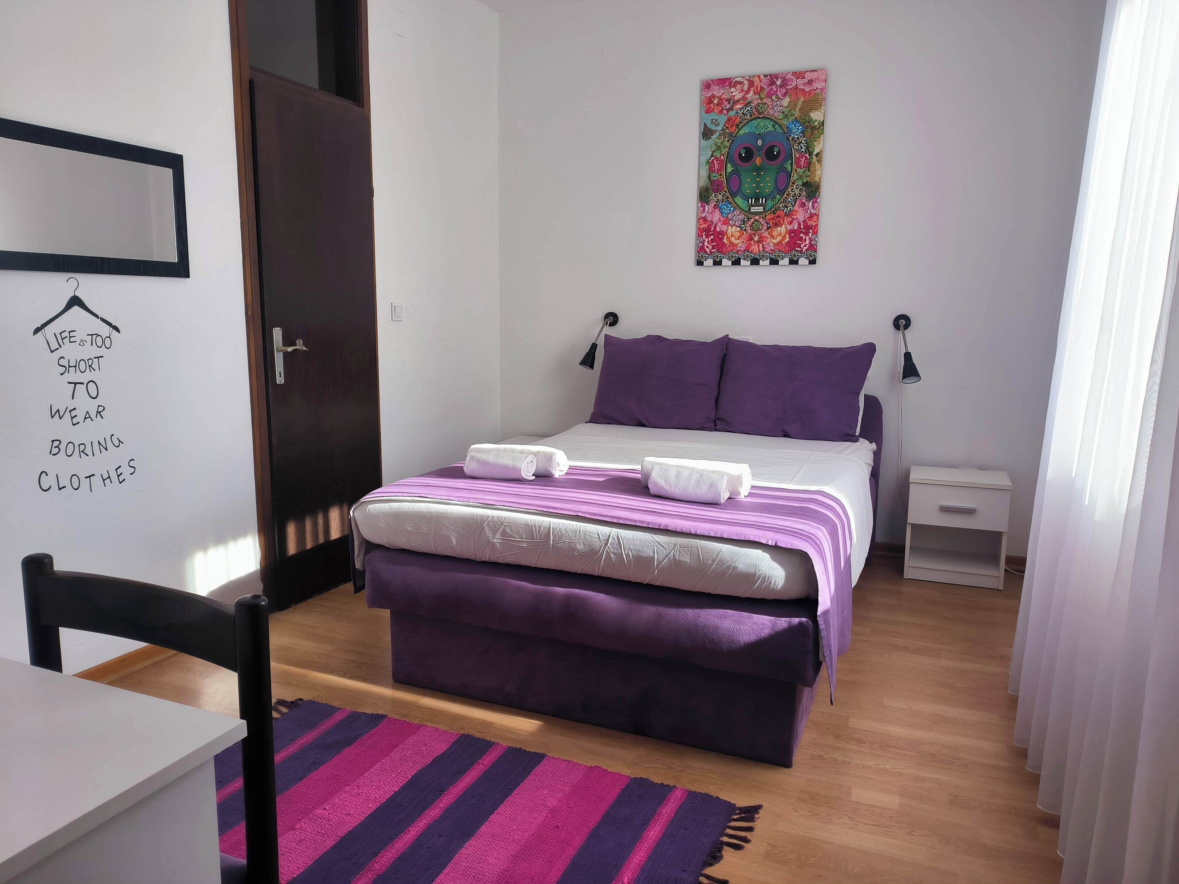 A bedroom with a bed, a nightstand, a chair, a desk, and a wall with a poster.
