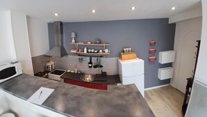 A compact kitchen with a microwave, stove, sink, and wooden shelves.