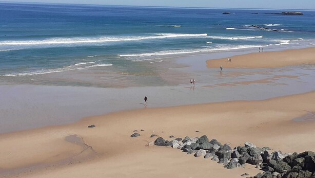 A beach with clear skies, calm waves, and a few people walking.