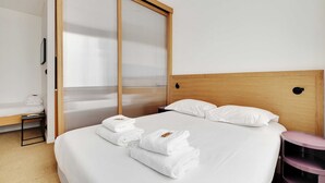 A hotel room with a bed, a wooden headboard, a bedside table, a small stool, and a sliding door with a view. - Beautiful Apartment 1br/3p - Marais/republique (Paris)