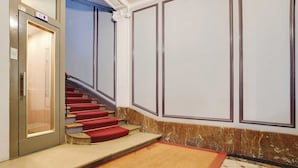 A hotel lobby with a marble floor, a red carpeted staircase, and a wall with paneling. - Beautiful Apartment 1br/3p - Marais/republique (Paris)