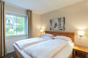 A hotel room with a large bed, two bedside lamps, a painting on the wall, and a window with curtains. - Familienhaus in Dierhagen (Ostseebad Dierhagen)