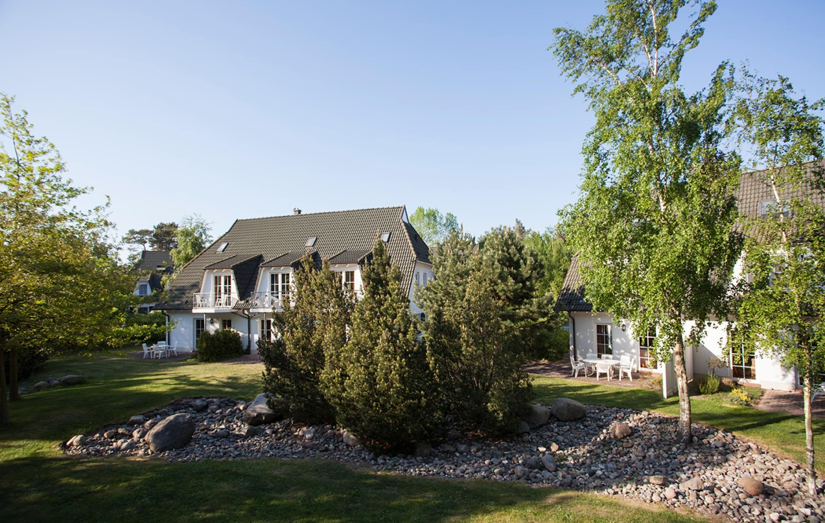 A two-story house with a sloped roof, surrounded by a well-maintained lawn and a small rock garden.