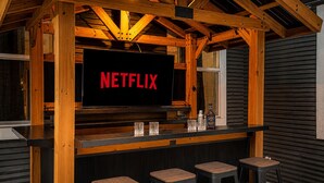 A wooden bar area with a Netflix sign, three stools, and a bottle on the counter.