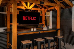 Una zona con barra de madera, un letrero de Netflix, tres taburetes y una botella sobre la encimera.