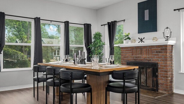 A dining area with a long wooden table, black chairs, and a brick fireplace.