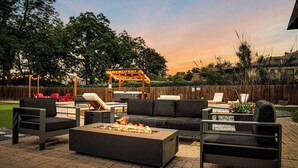 An outdoor patio with a fire pit, lounge chairs, and a wooden pergola.