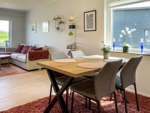 Un comedor con una mesa y sillas de madera, un sofá, una estantería y una ventana con jarrones decorativos.