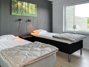 A modern bedroom with two beds, a wall-mounted artwork, and a window with a view.