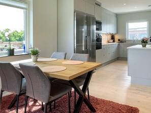 A modern kitchen with a dining area, featuring a wooden table with chairs, a large refrigerator, and a view of the outdoors. - 5 Star Holiday Home in Morbylanga (Morbylanga)