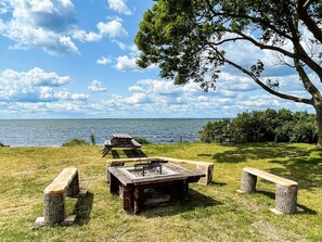 A picnic area with a wooden table and benches, surrounded by trees and a view of the water. - 5 Star Holiday Home in Morbylanga (Morbylanga)