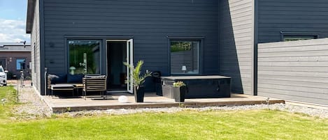 Ein modernes Haus mit einer Terrasse, Sitzgelegenheiten im Freien und einem großen Fenster.