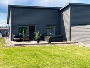 Ein modernes Haus mit einer Terrasse, Sitzgelegenheiten im Freien und einem großen Fenster.