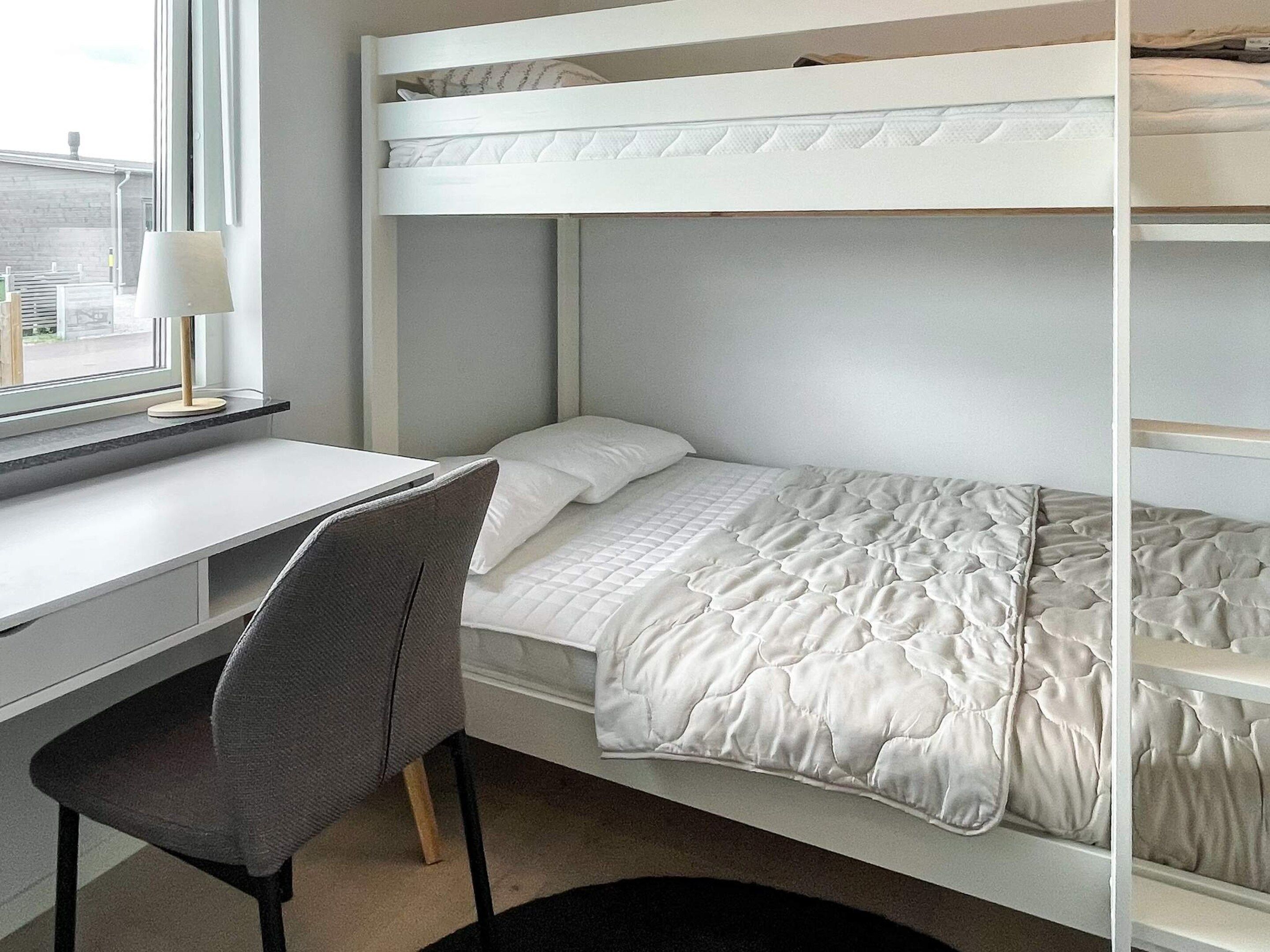 A bunk bed with a desk and chair, a window with a view, and a bedside table.