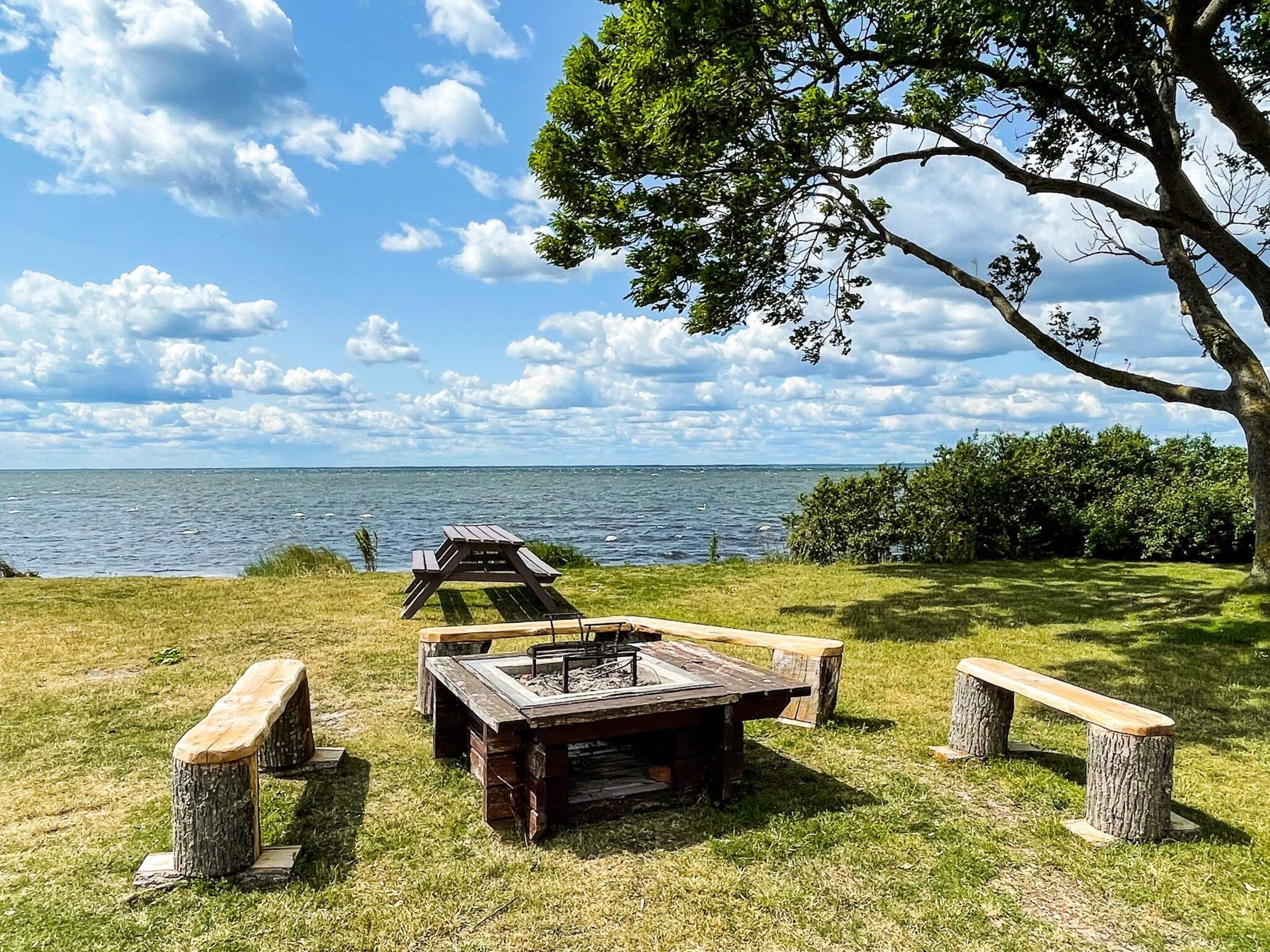 A picnic area with a wooden table and benches, surrounded by trees and a view of the water.