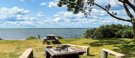 A picnic area with a wooden table and benches, surrounded by trees and a view of the water.