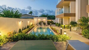 Una piscina con sillas de descanso, rodeada de vegetación y un edificio moderno con balcones.