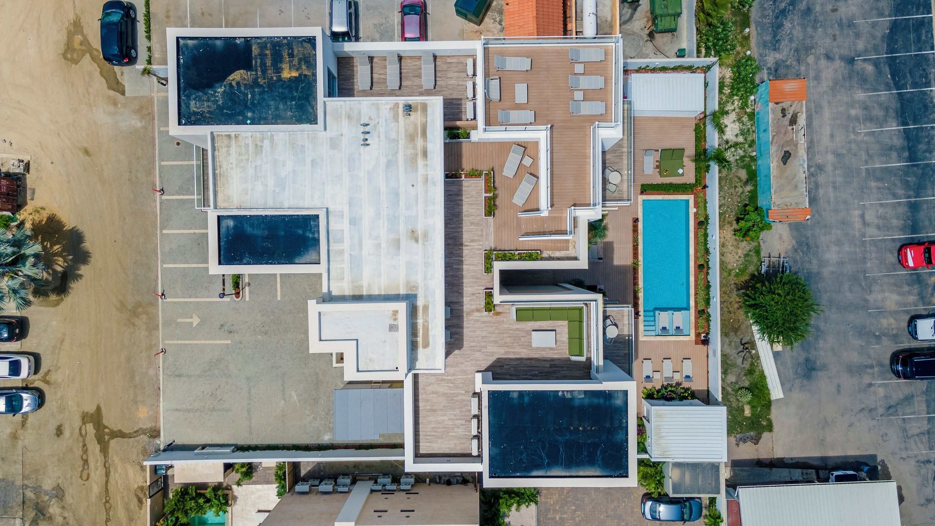 An aerial view of a hotel with multiple swimming pools, a parking lot, and a beach area.