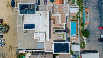 An aerial view of a hotel with multiple swimming pools, a parking lot, and a beach area.