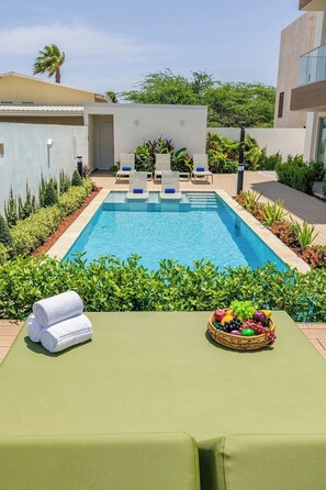 Un área junto a la piscina con sillones de descanso, una piscina y una mesa con toallas y fruta.
