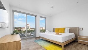 Un dormitorio moderno con una cama grande, un escritorio de madera y vistas a la ciudad a través de amplias ventanas.