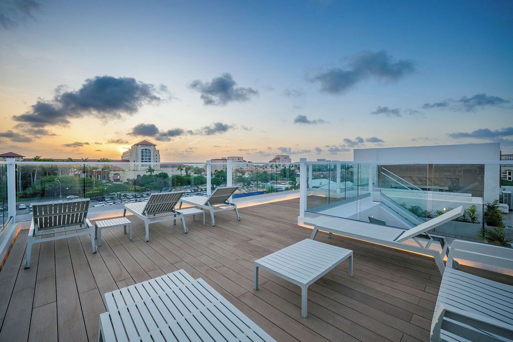 Una terraza en la azotea con suelo de madera, sillones blancos para lounge y mesas.
