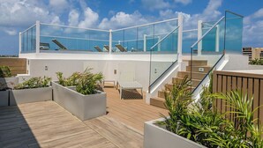 Una terraza moderna en la azotea con barandas de vidrio, mobiliario exterior y jardineras.