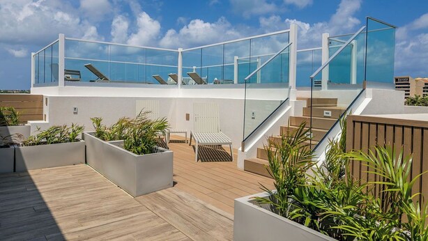 Una terraza moderna en la azotea con barandas de vidrio, mobiliario exterior y jardineras.