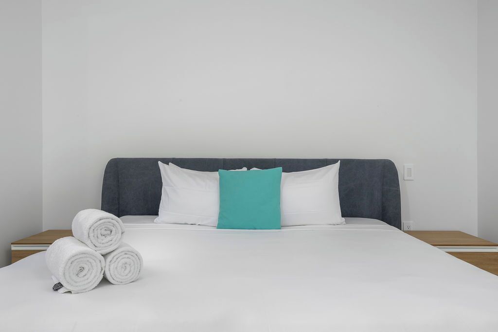 Un letto rifatto con lenzuola bianche e un cuscino color acquamarina, affiancato da asciugamani bianchi arrotolati.
