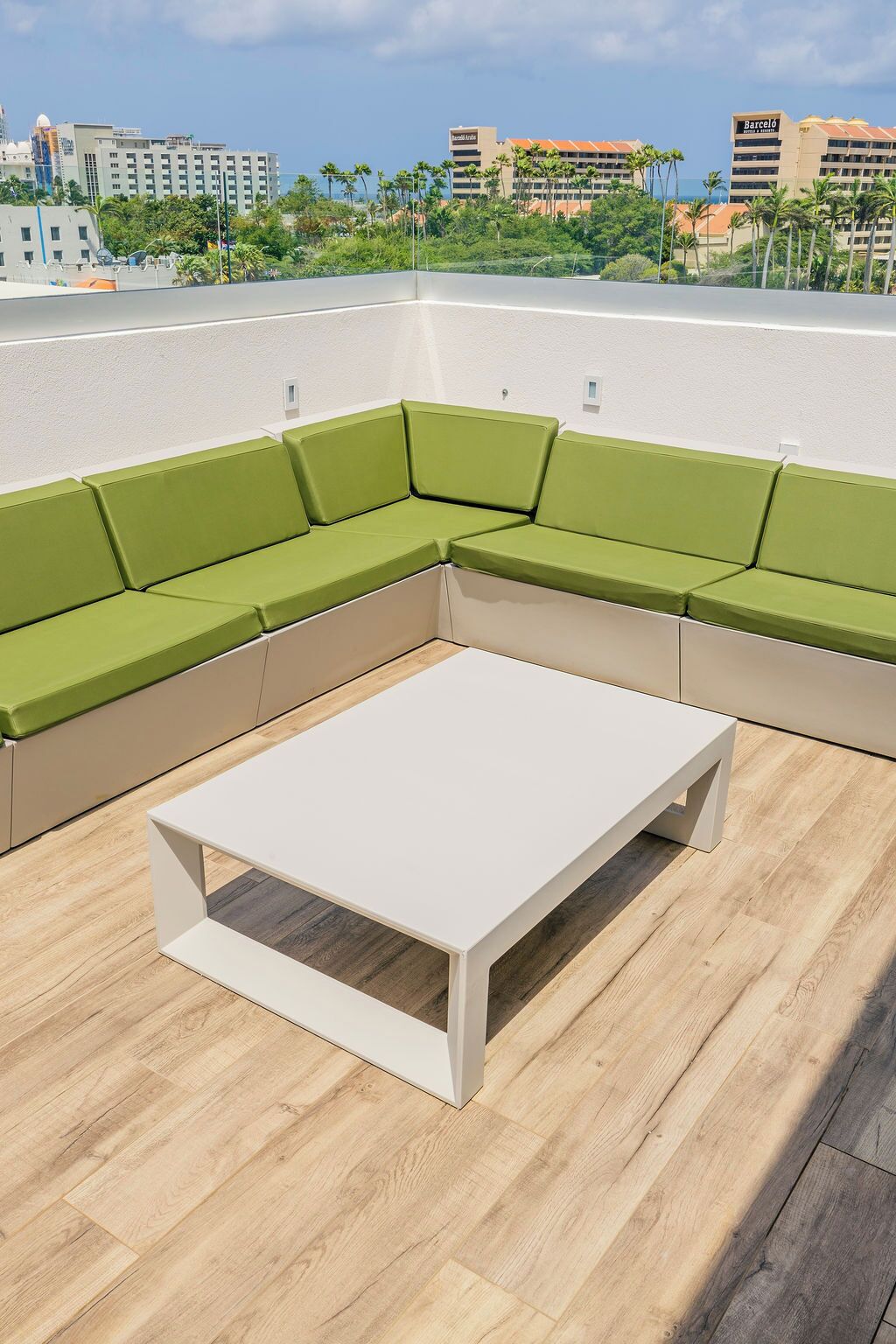 A rooftop terrace with a green cushioned seating area and a white table.