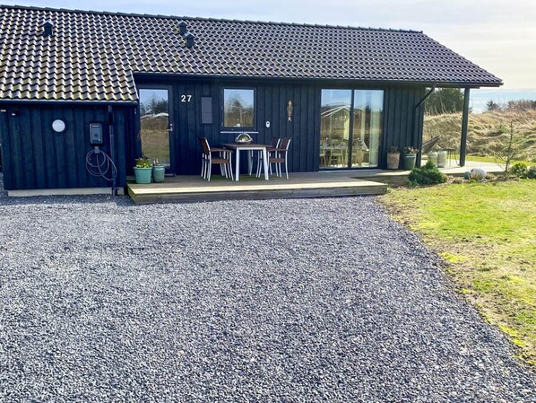 Een modern gebouw met een pannendak, het cijfer '27' aan de zijkant en een grindpad dat leidt naar een terras met buitenmeubels.