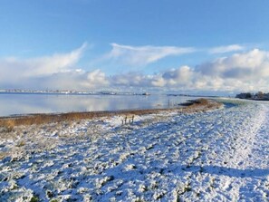 A snow-covered landscape with a frozen body of water, a clear sky, and distant buildings. - 5 Star Holiday Home in Hirtshals (Hirtshals)