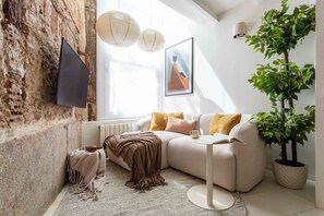 A modern living room with a stone wall, a sofa, a coffee table, a potted plant, and a flat-screen TV.