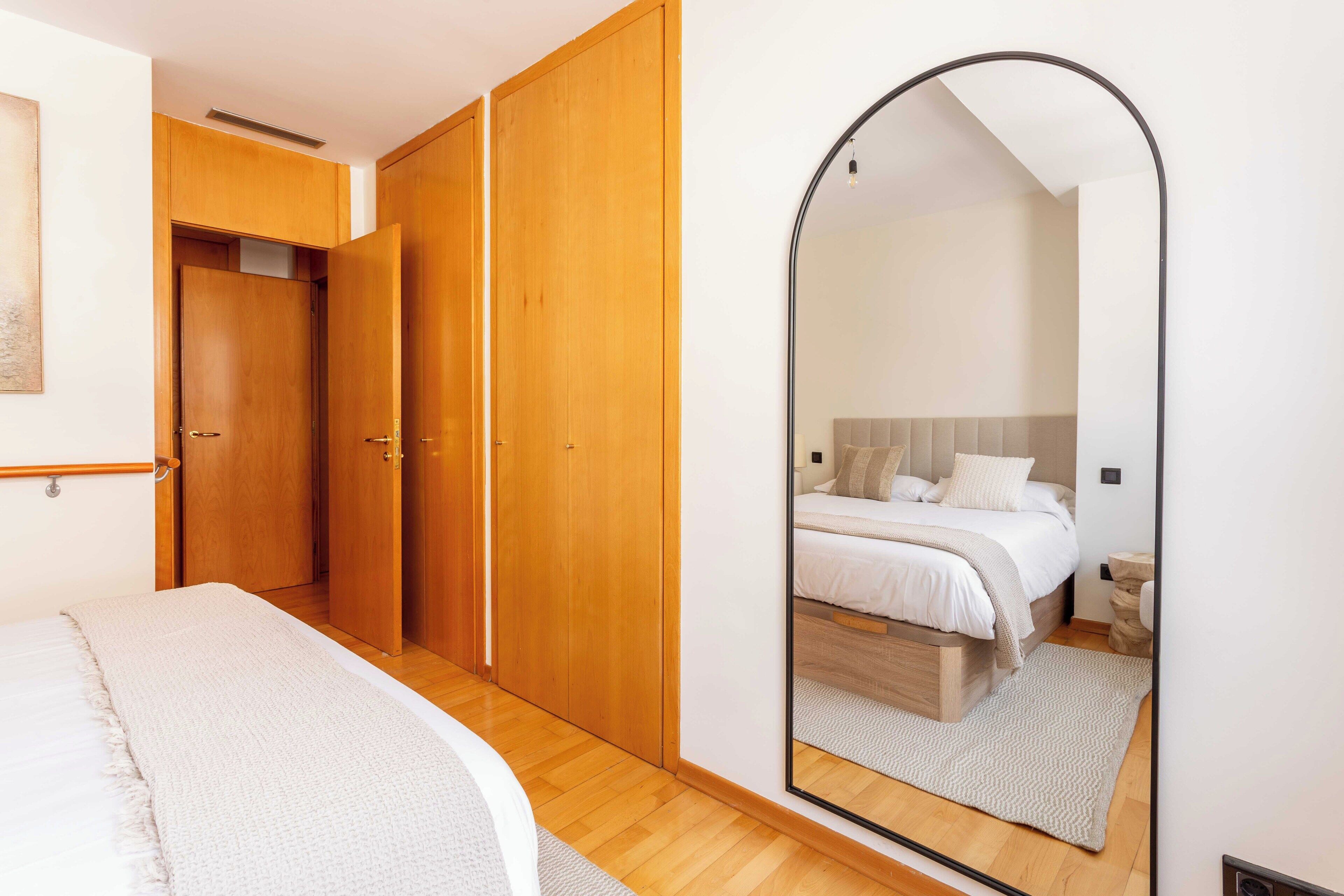 Une chambre avec une armoire en bois, un grand miroir et un lit doté d’une tête de lit blanche.