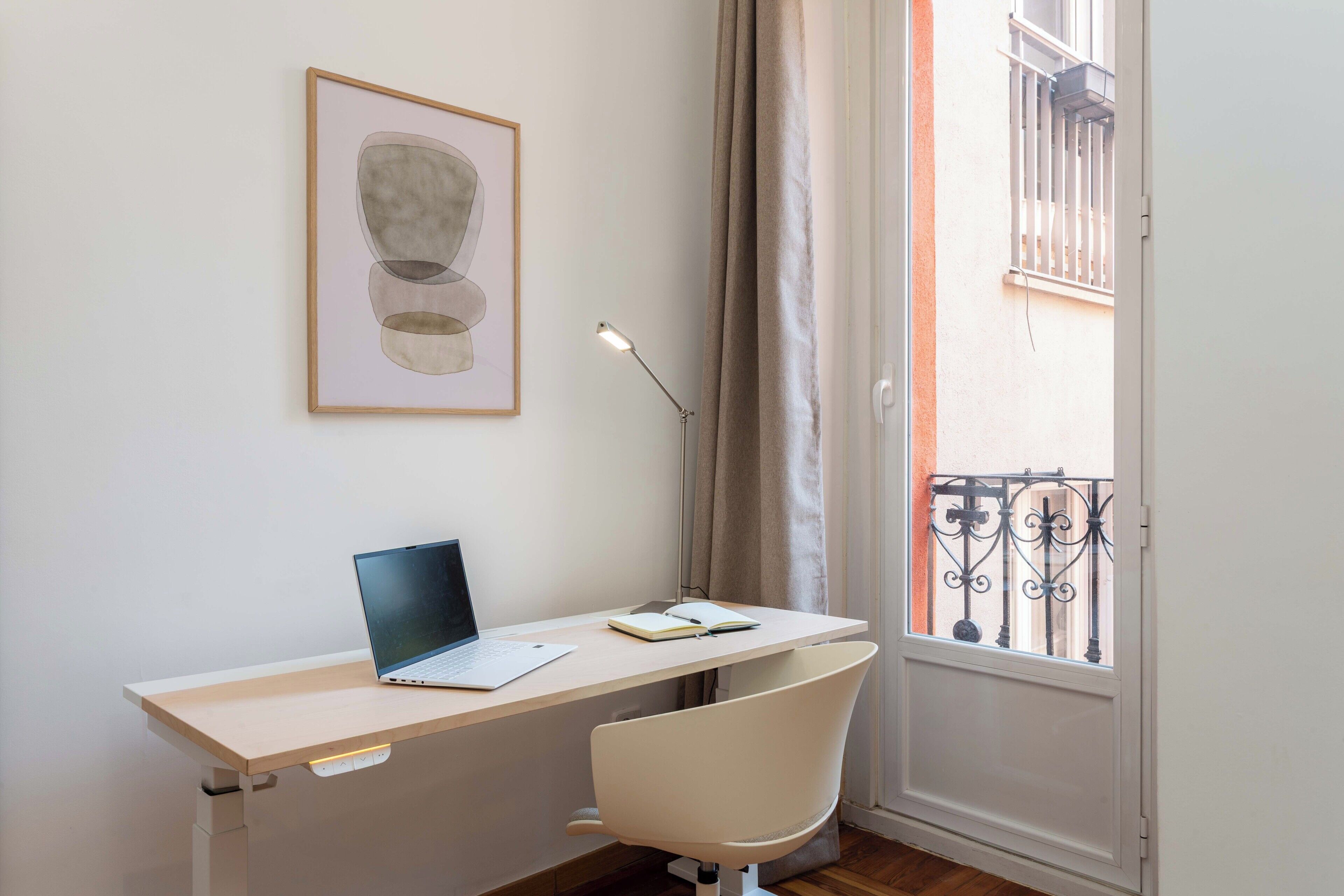 Ein Arbeitsplatz mit Schreibtisch, Stuhl, Laptop und einem gerahmten Bild an der Wand.
